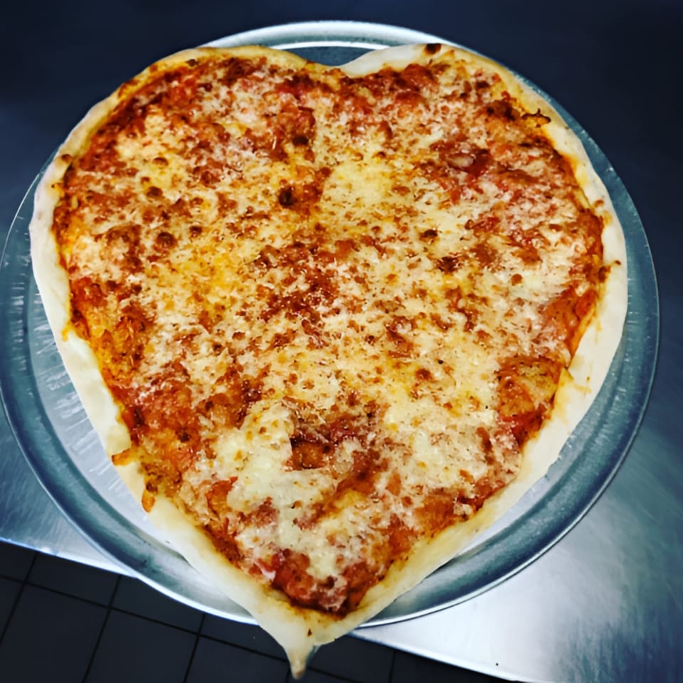 A heart-shaped cheese pizza from Nick's Pizza & Ice Cream, on a metal pizza pan.
