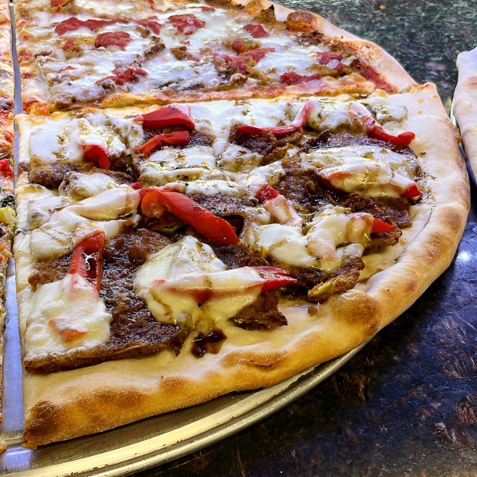Two large slices of Nick's Pizza with melted cheese, red peppers, and meat on a metal tray.
