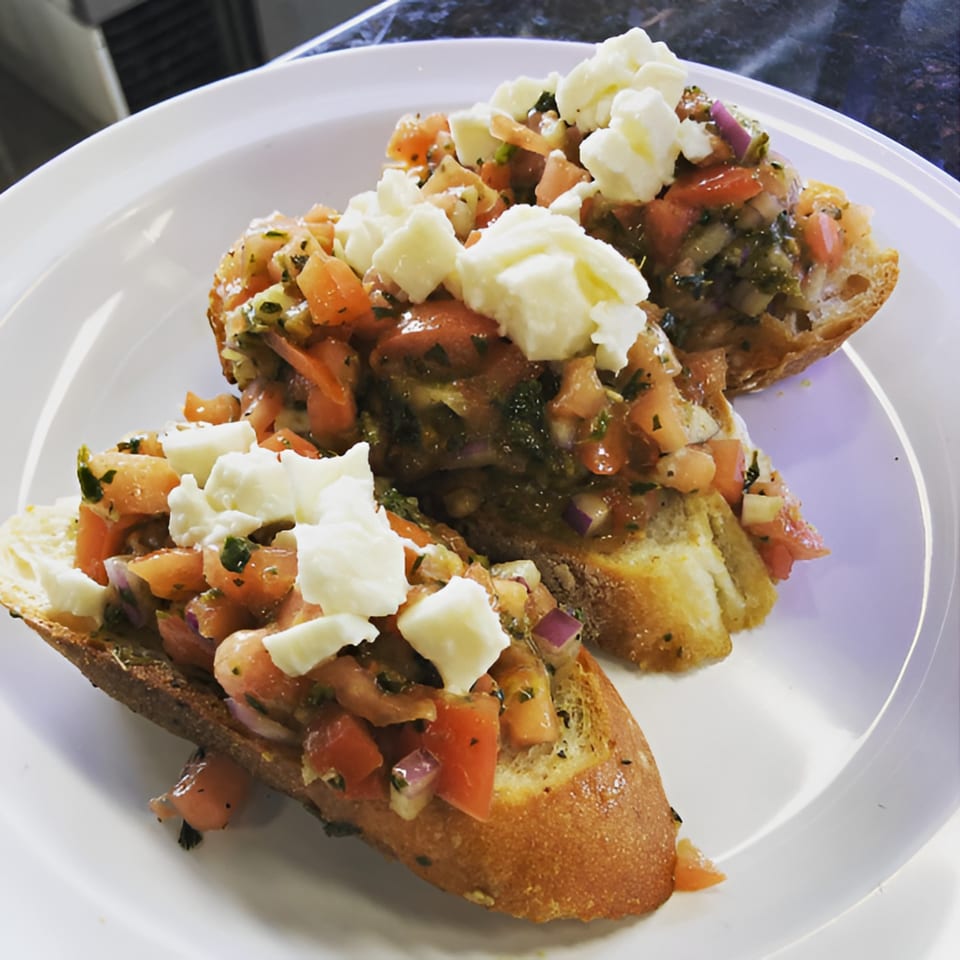 Three pieces of bruschetta topped with diced tomatoes, red onion, herbs, and fresh mozzarella.